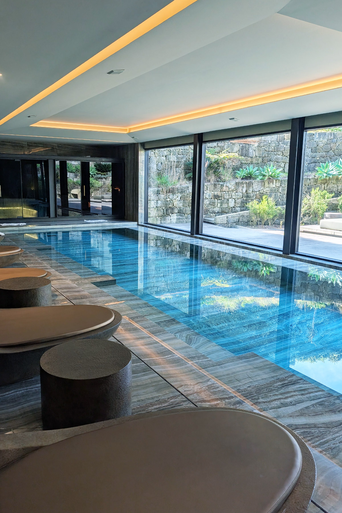 Indoor swimming pool with stone seating and large windows.