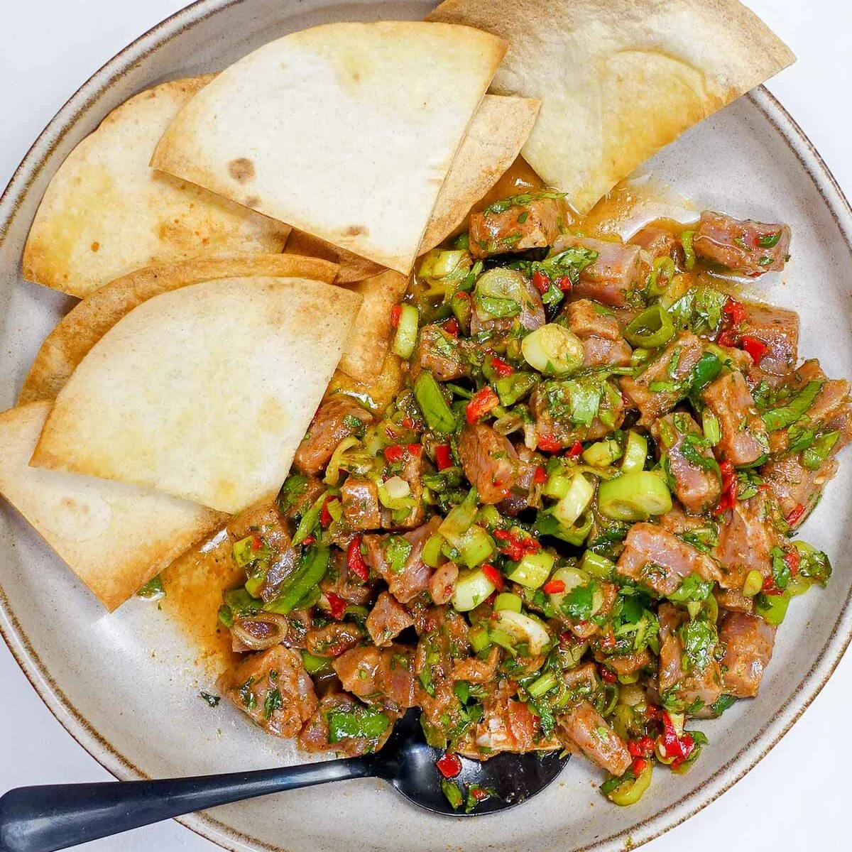 Mediterranean tuna tartare with chopped herbs and pita chips on a plate.