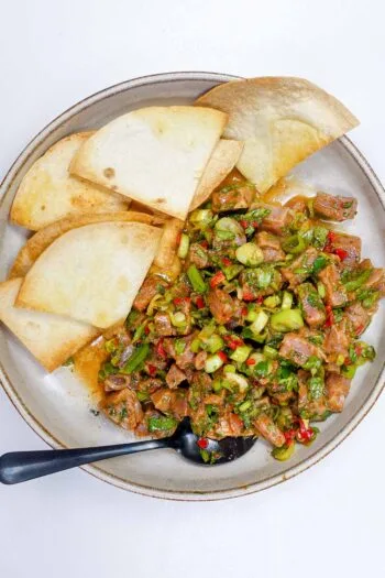 Mediterranean tuna tartare with chopped herbs and pita chips on a plate.