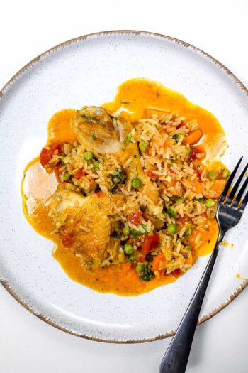 Portuguese chicken rice with peas, carrots, and tomato sauce on white plate.