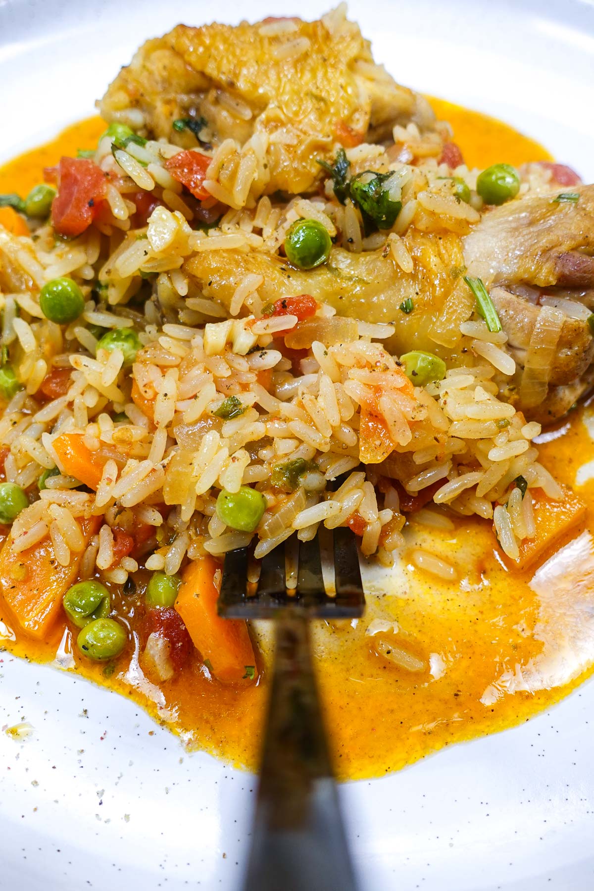 Portuguese chicken rice with peas, carrots, and tomato sauce on white plate.