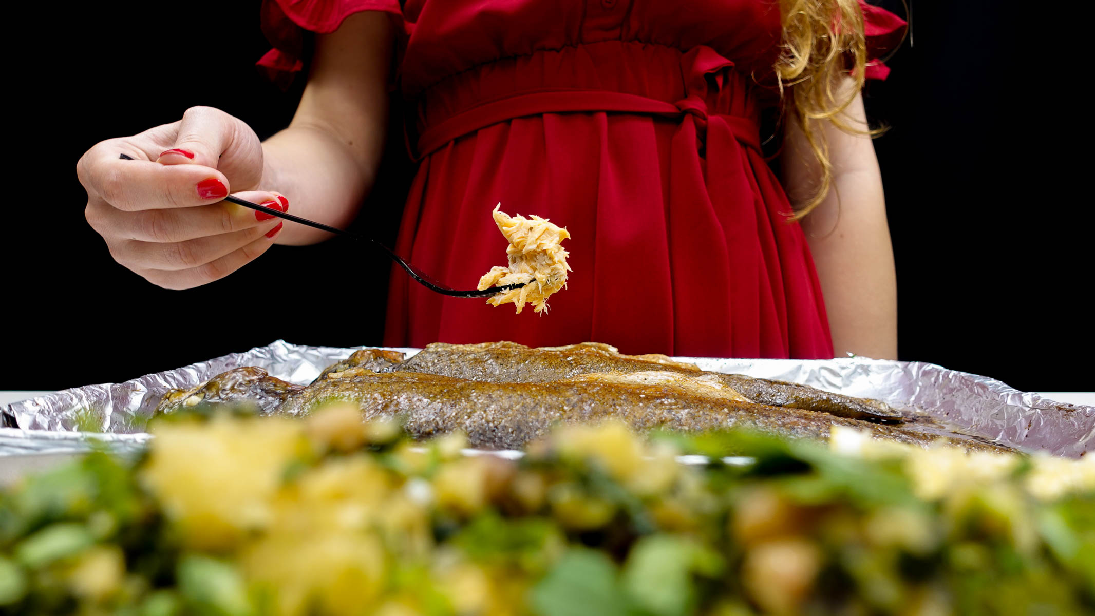 Helena in red dress holding fork with baked whole rainbow trout.