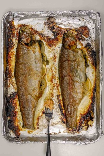 Two whole baked rainbow trout on foil-lined tray with fork.