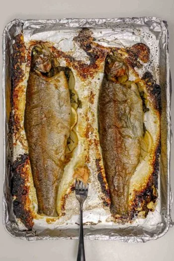 Two whole baked rainbow trout on foil-lined tray with fork.