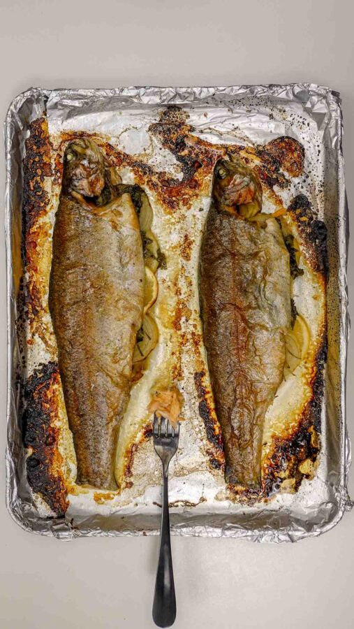 Two whole baked rainbow trout on foil-lined tray with fork.