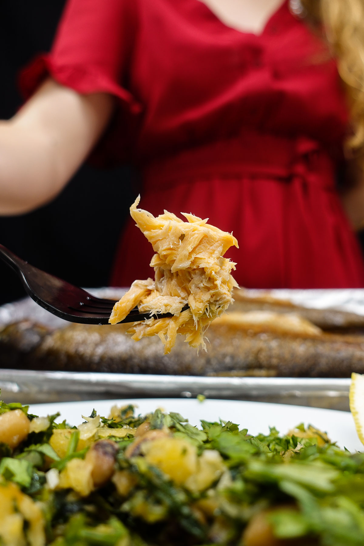 Fork holding flaky cooked rainbow trout with greens and potatoes.