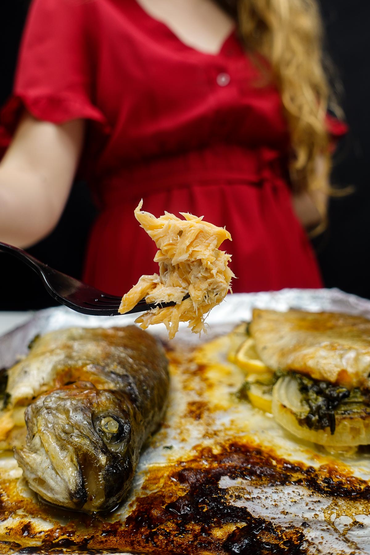Baked whole rainbow trout with flaky cooked fish on fork.