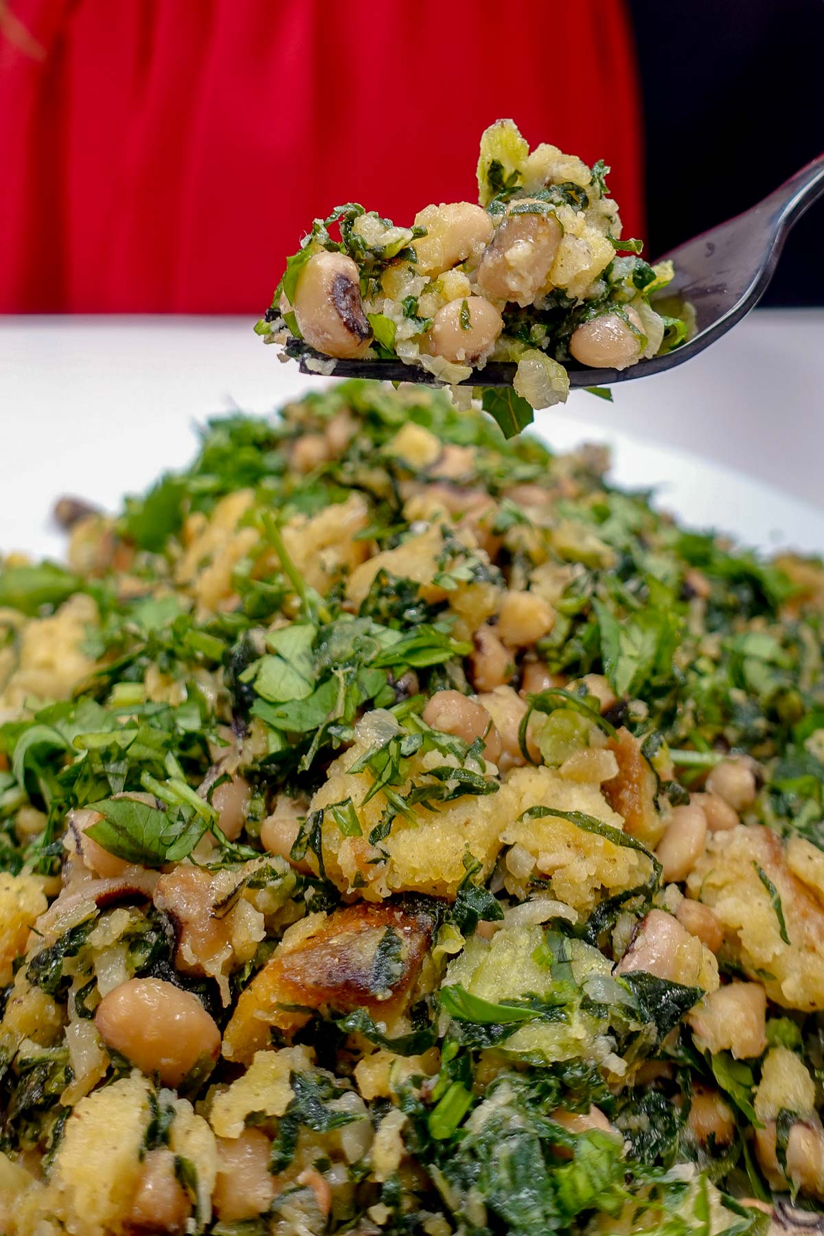 Black-eyed peas mixed with bread pieces and fresh herbs on a fork.