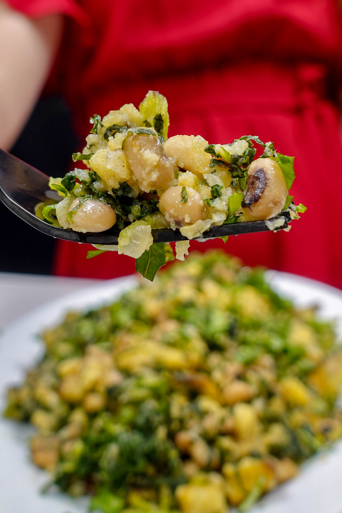 Close-up of black-eyed peas bread mash with greens on a fork.