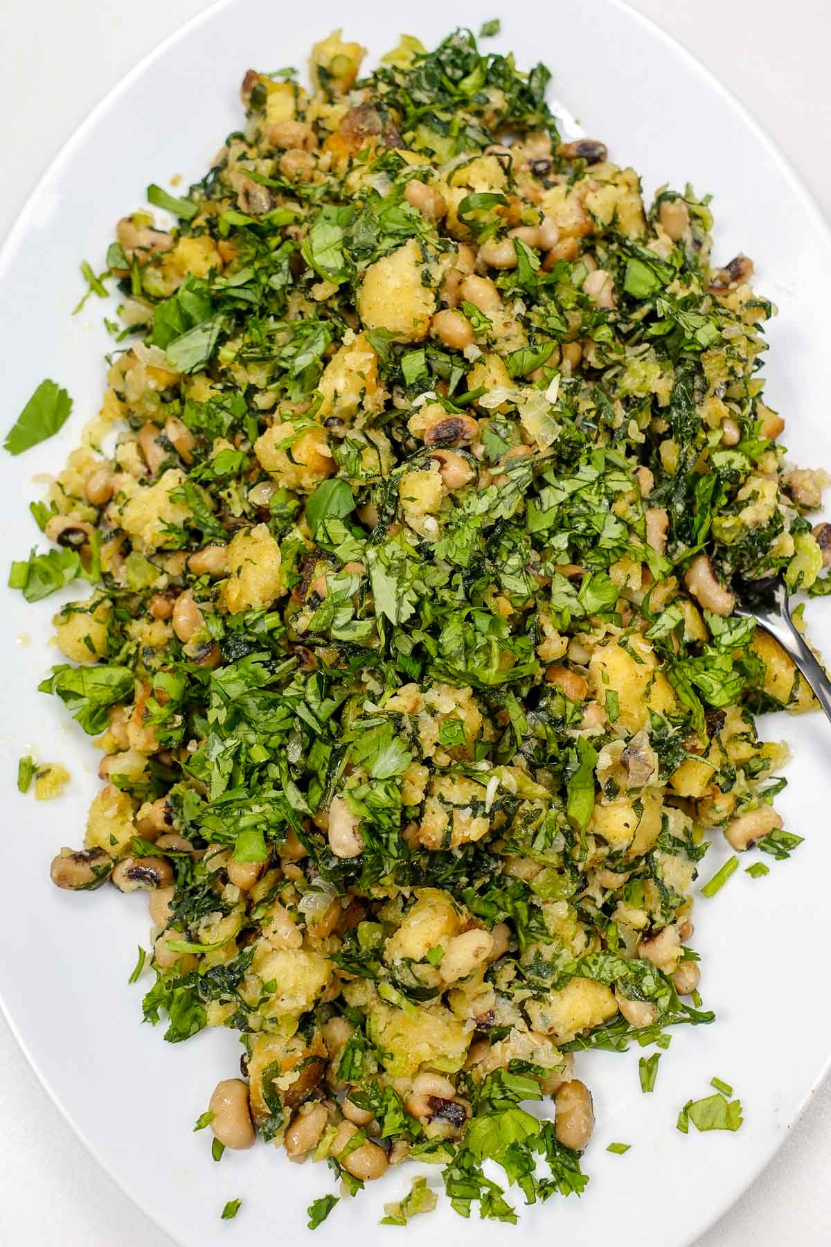 Black-eyed peas and bread mash with fresh chopped greens on white plate.