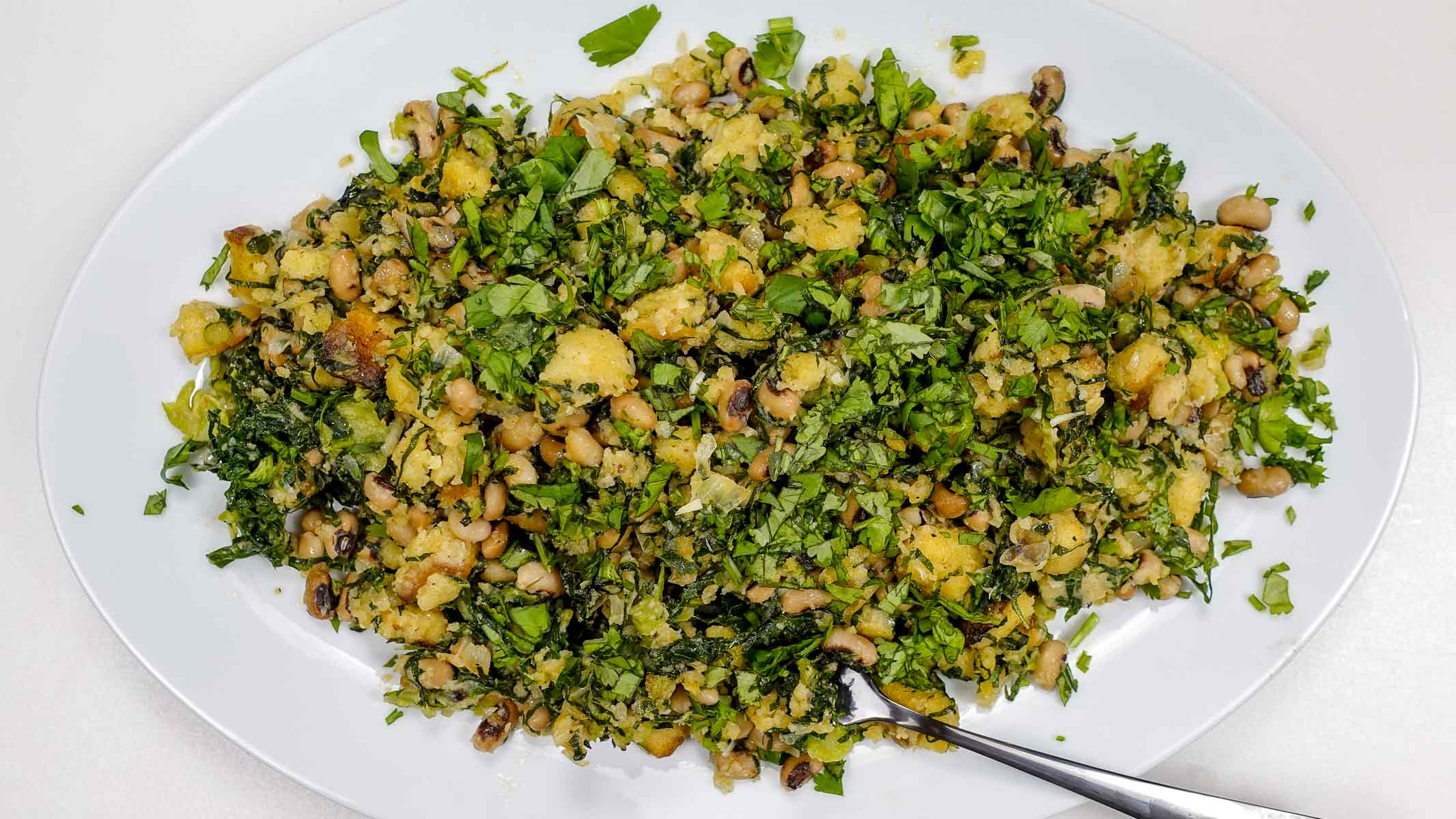 Black-eyed peas bread mash with chopped greens on white plate.