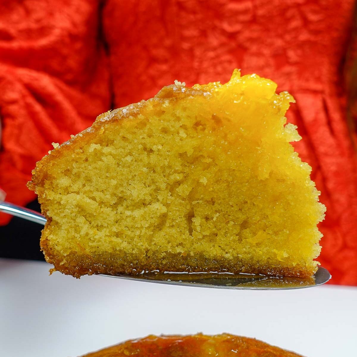 Slice of moist Portuguese orange cake with syrup held above whole cake.