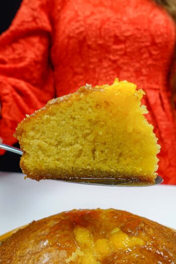 Slice of moist Portuguese orange cake with syrup held above whole cake.