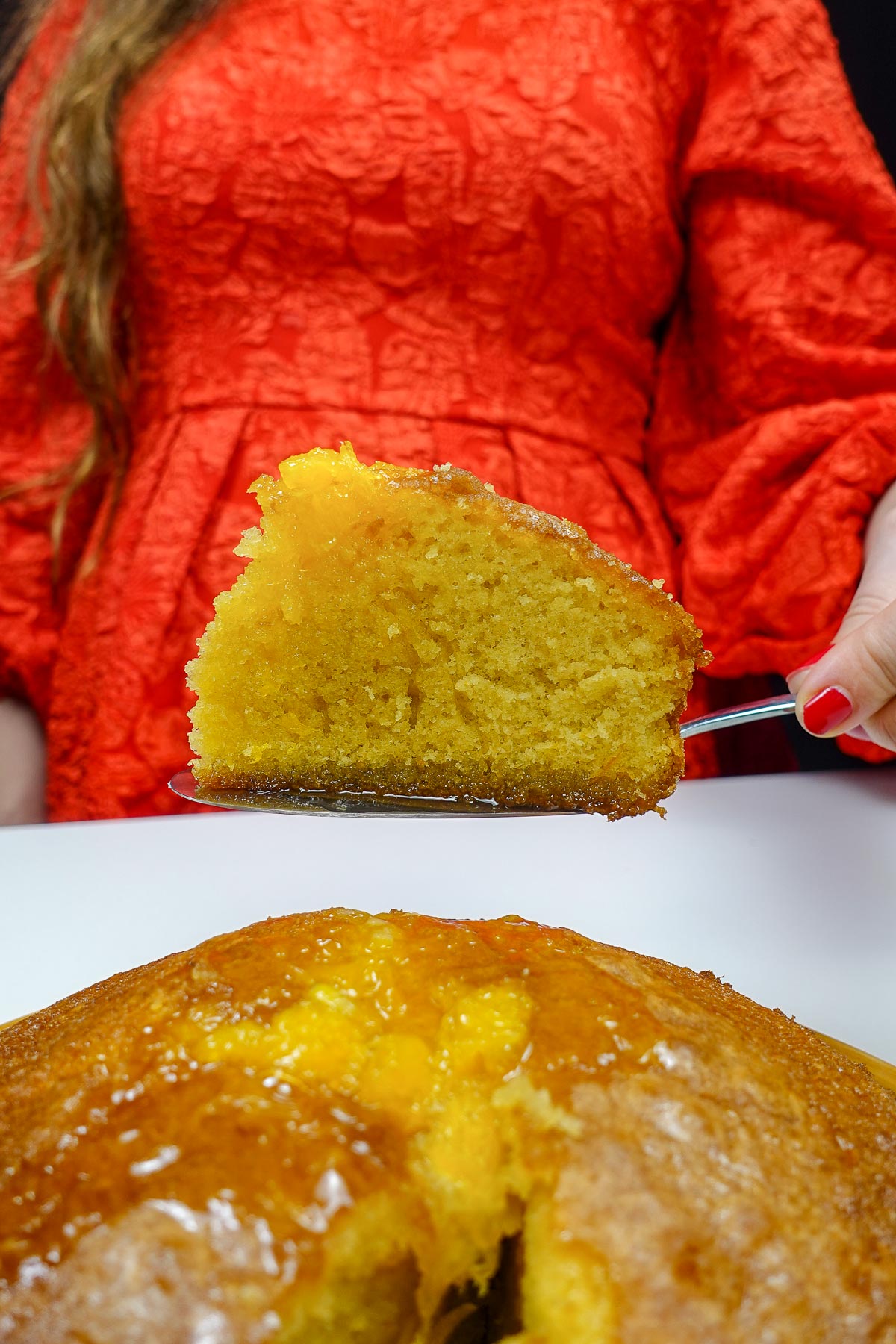 Slice of moist Portuguese orange cake held by Helena in red dress.