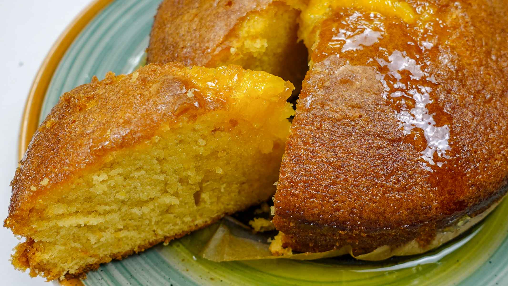 Moist Portuguese orange cake with a glossy top on a green plate.