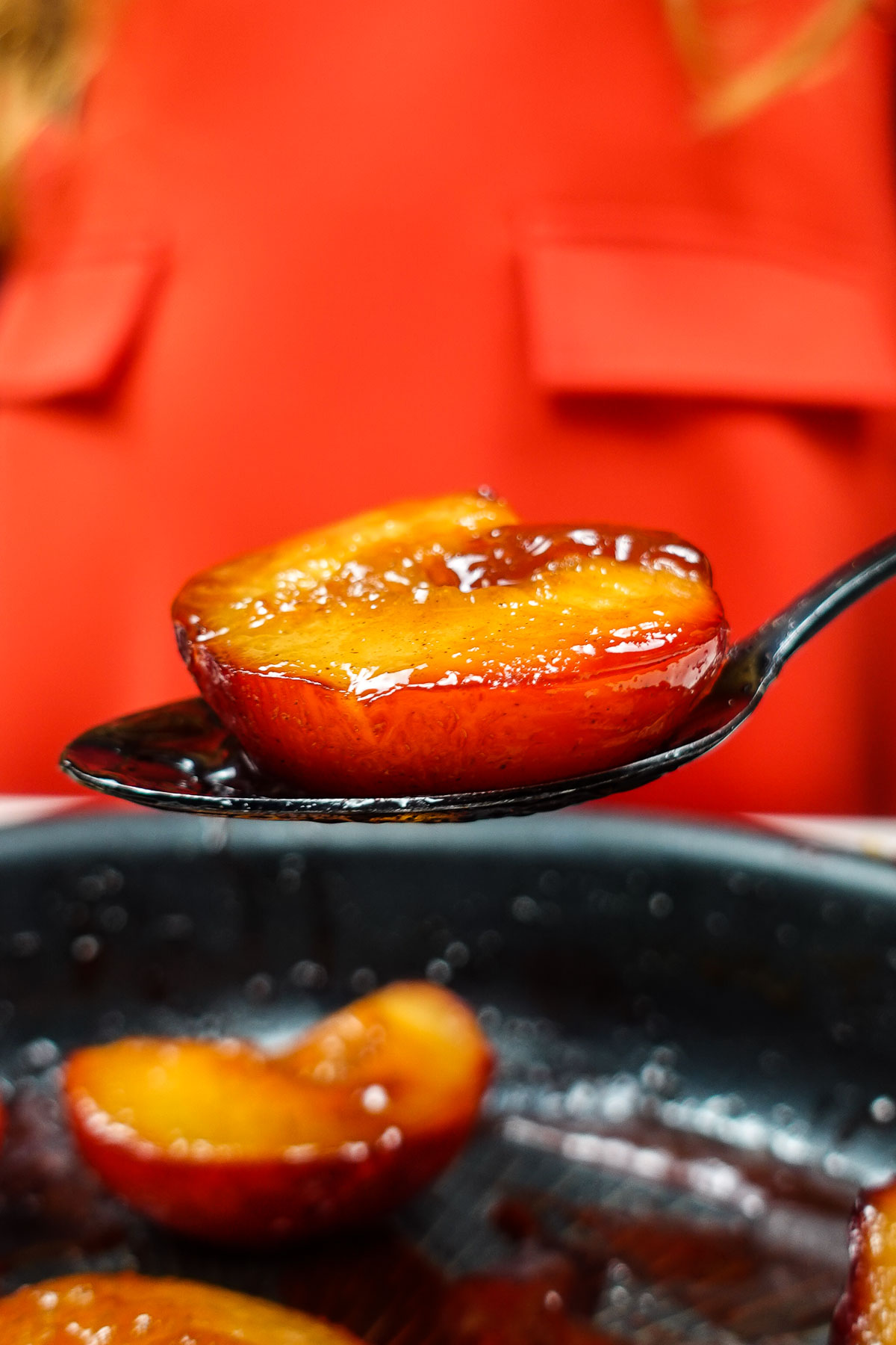 Caramelized plum half on a spoon with a red background.