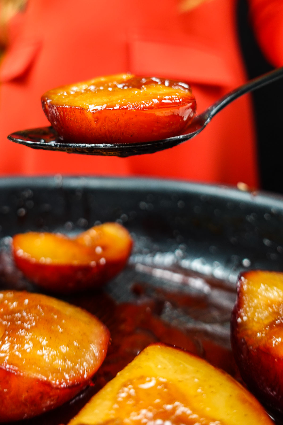 Caramelized plum half on a spoon above a pan with more plums.