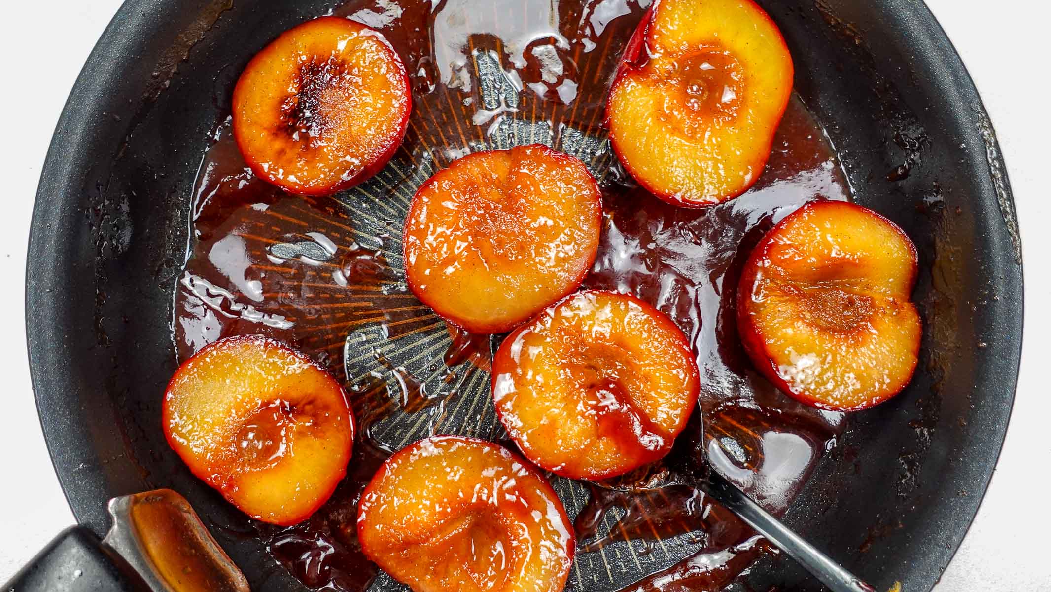Caramelized plum halves cooking in a black skillet with syrup.