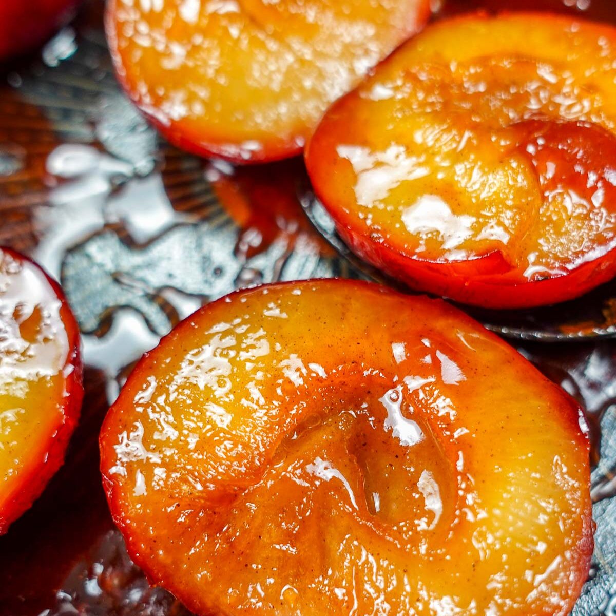 Caramelized plum halves with syrup on a dark surface.