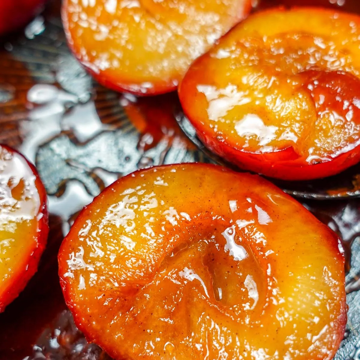 Caramelized plum halves with syrup on a dark surface.