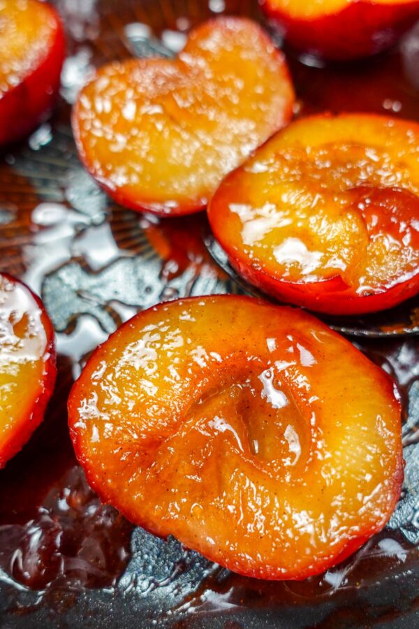 Caramelized plum halves with syrup on a dark surface.