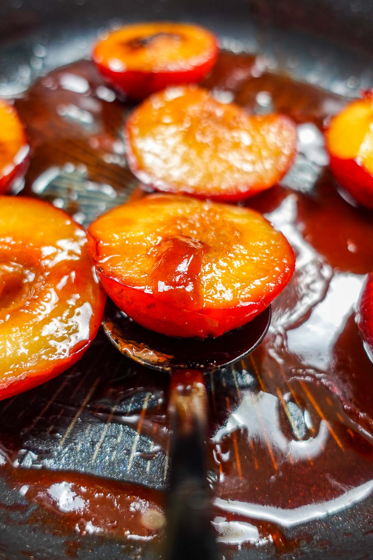 Caramelized plum halves cooking in a pan with syrup.