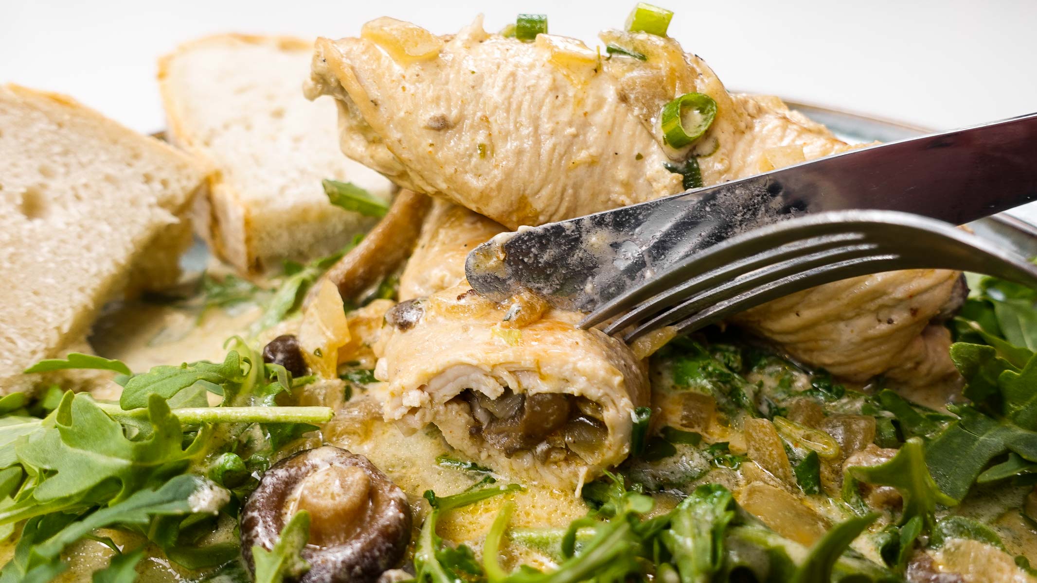 Turkey roulades stuffed with mushrooms served with greens and bread slices.