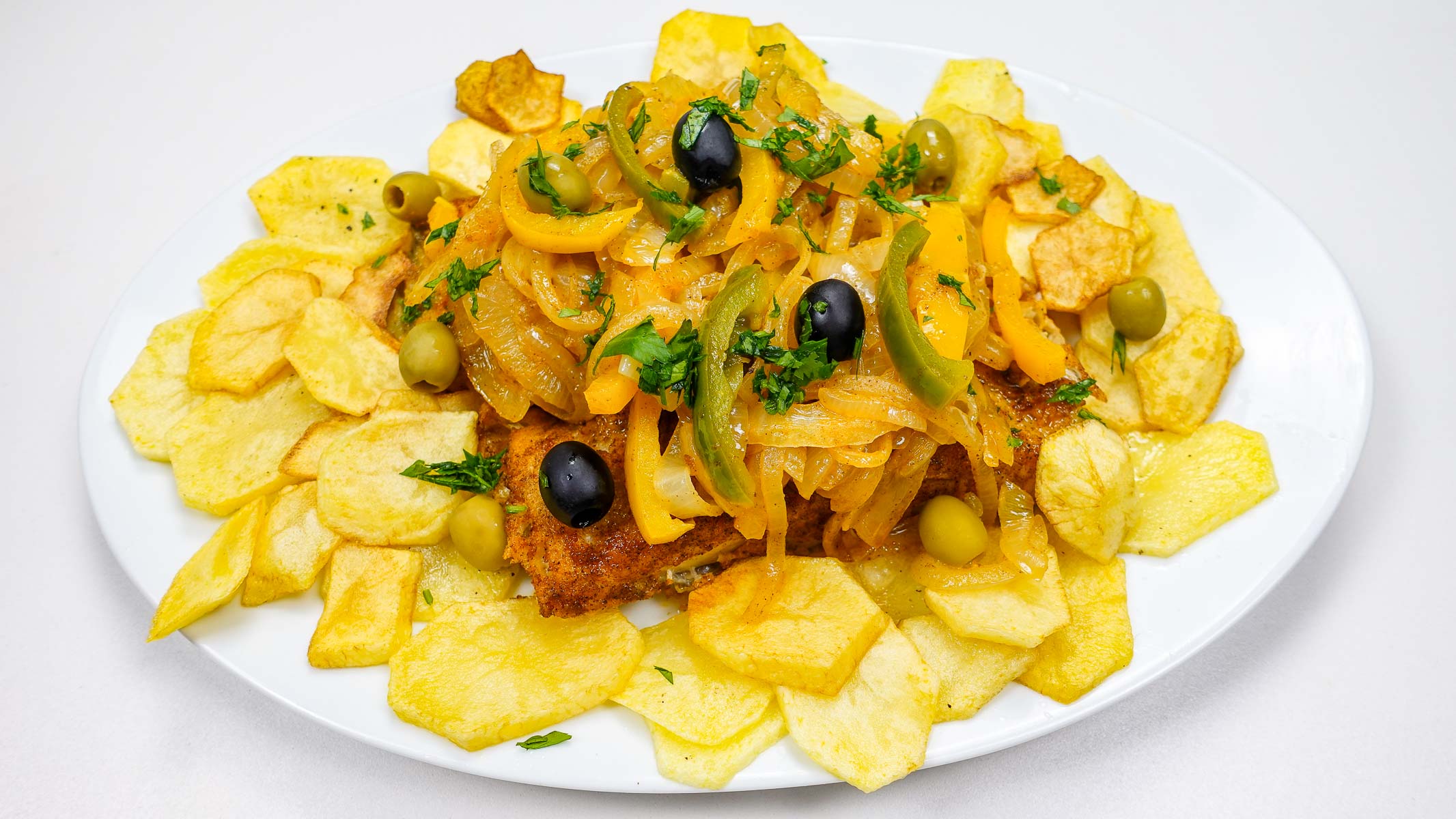 Crispy fried cod topped with sautéed onions, peppers, and olives on potato slices.