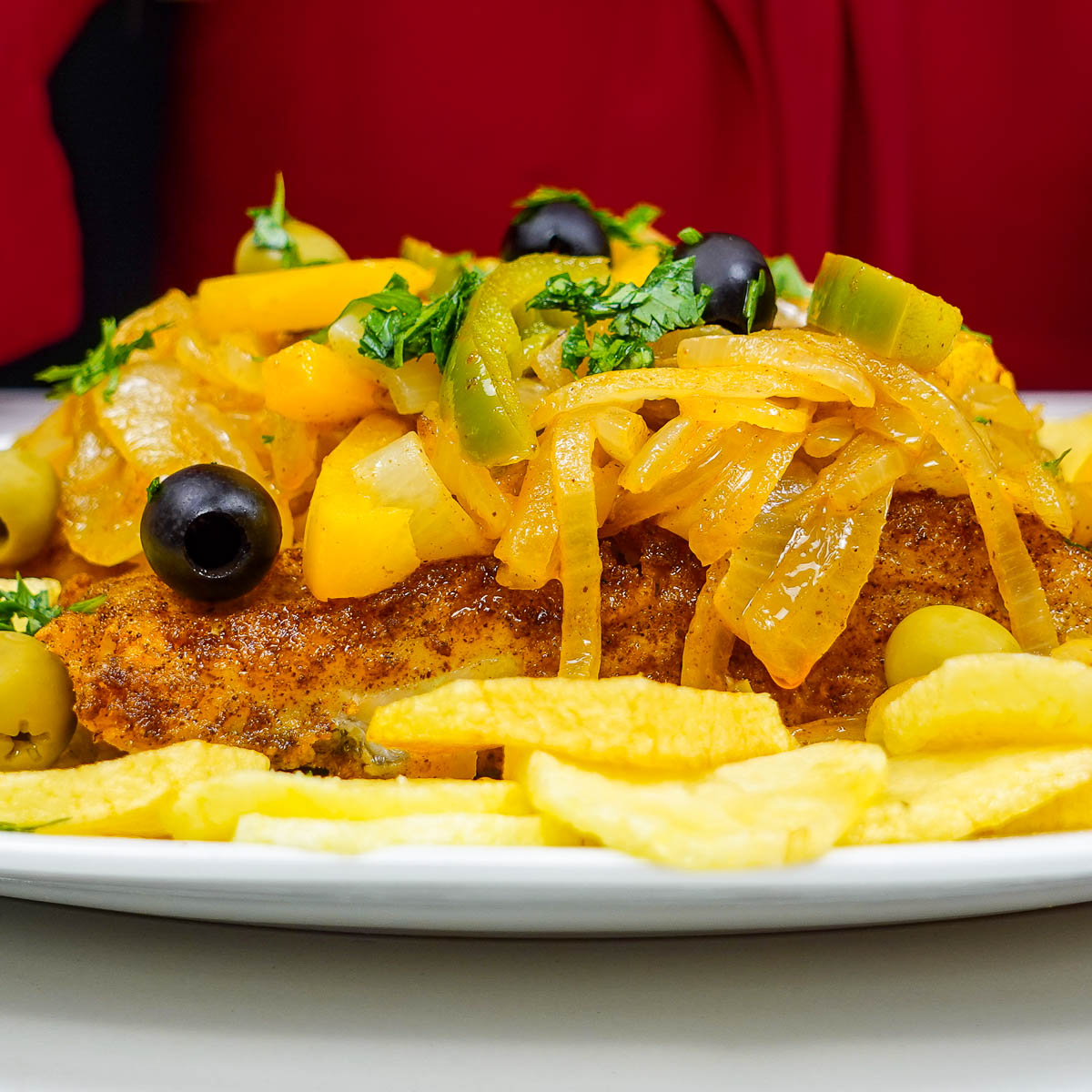 Crispy fried cod topped with sautéed onions, peppers, and olives with fries.